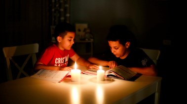 طفلان يراجعان دروسهما في ضوء الشموع بسبب انقطاع الكهرباء