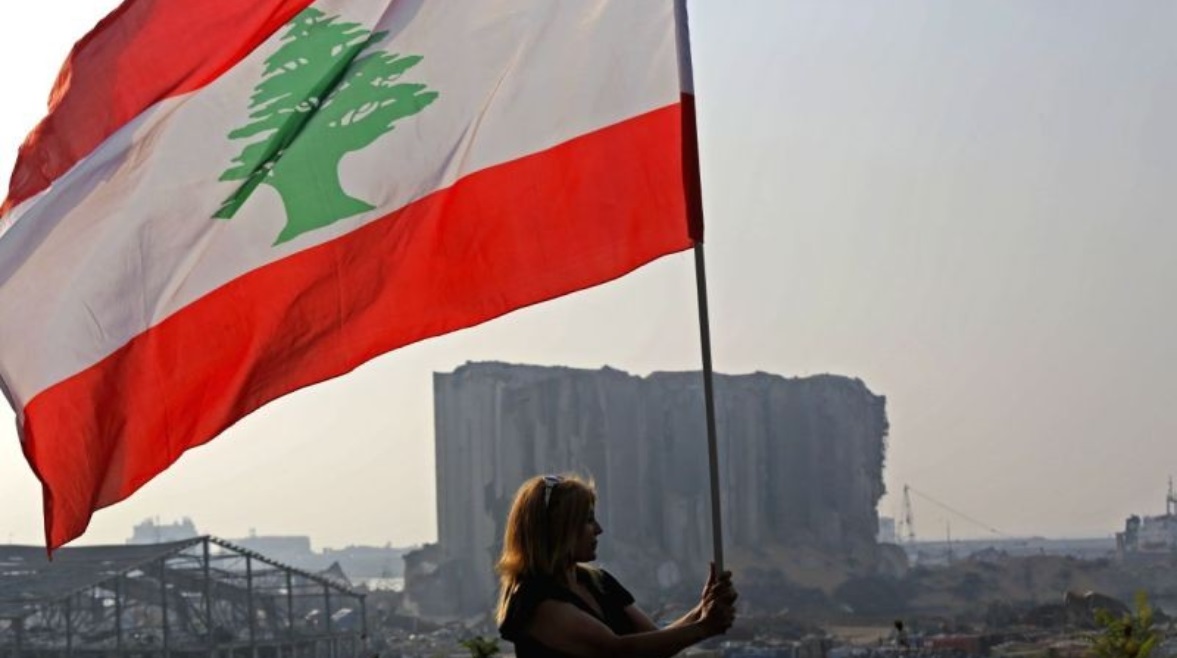 سيدة لبنانية تحمل علم بلادها أمام حطام مرفأ بيروت 