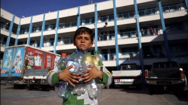 أحد أطفال غزة النازحين يحمل زجاجات بلاستيكية فارغة في أحد مدارس "الأونروا" والتي تحولت إلى مخيم يستقبل الاجئين