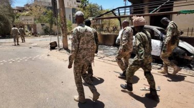 جنود من الجيش السوداني يسيرون بجوار مركبات عسكرية مدمرة بعد معركة مع "قوات الدعم السريع" في الخرطوم 