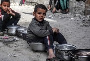 أطفال جالسون وبحوزتهم أواني فارغة ينتظرون فتات الطعام