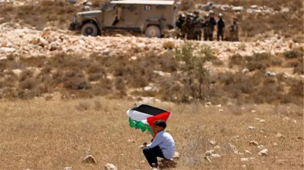 طفل فلسطيني يرفع علم فلسطين في وجه جنود الاحتلال